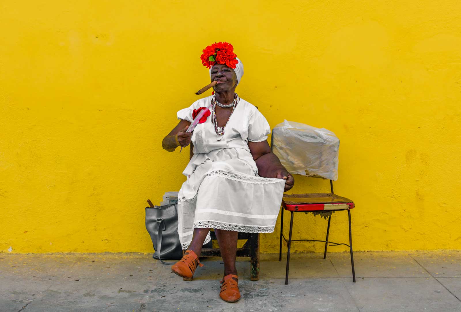 cuban woman in white dress with cigar sitting in front of yellow wall